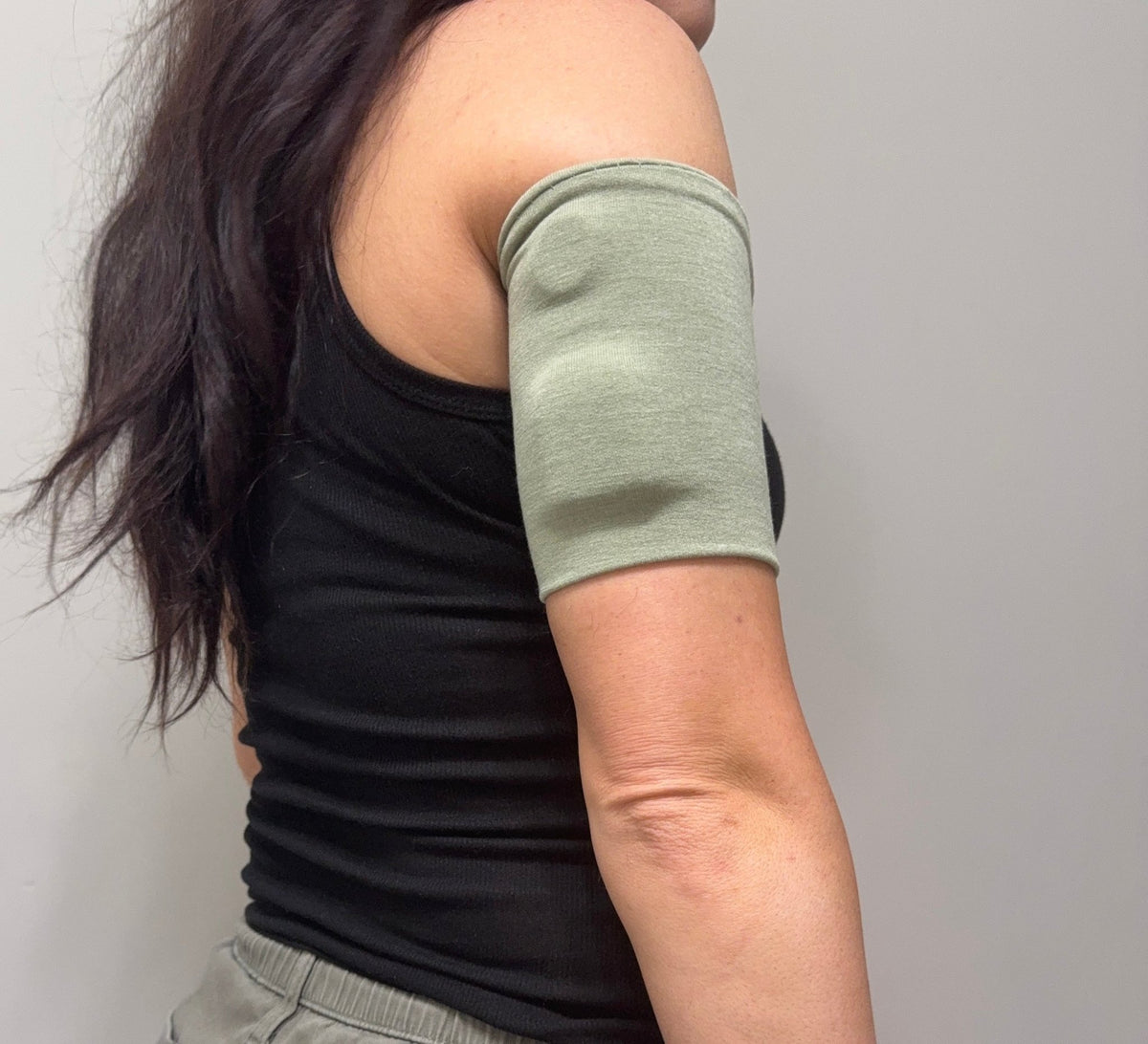 Soft cotton-feel pod band in Sage Green worn on the upper arm over a pod
